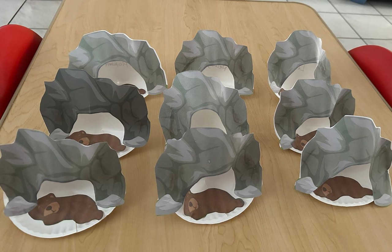 Paper-plate bear caves made by the children, drying on a table.