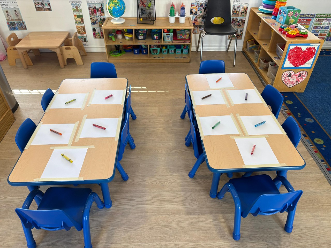 A KSW classroom set up for a morning of drawing — blue chairs, wooden tables, paper and crayons ready at each seat